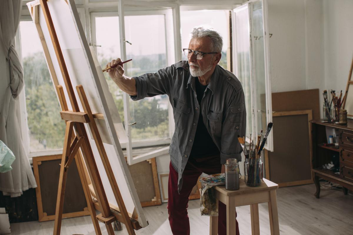 Older man painting on a canvas and easel