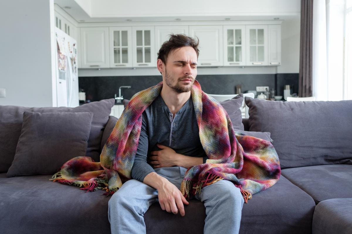 Man sitting on couch holding stomach sick