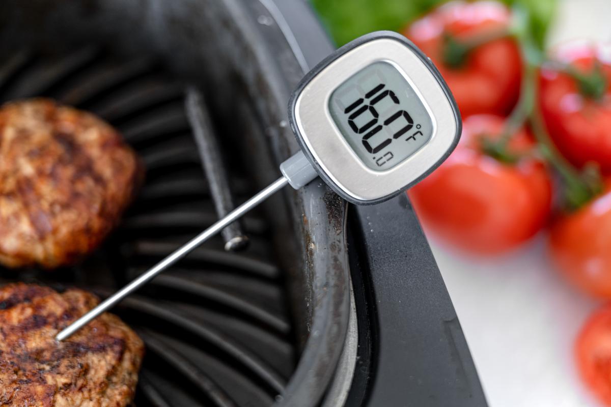 Probe thermometer at 160 degrees F in a burger on a grill