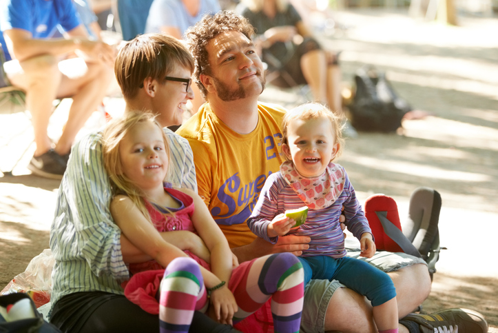 Parents and two young daughters sitting on the ground at a festival