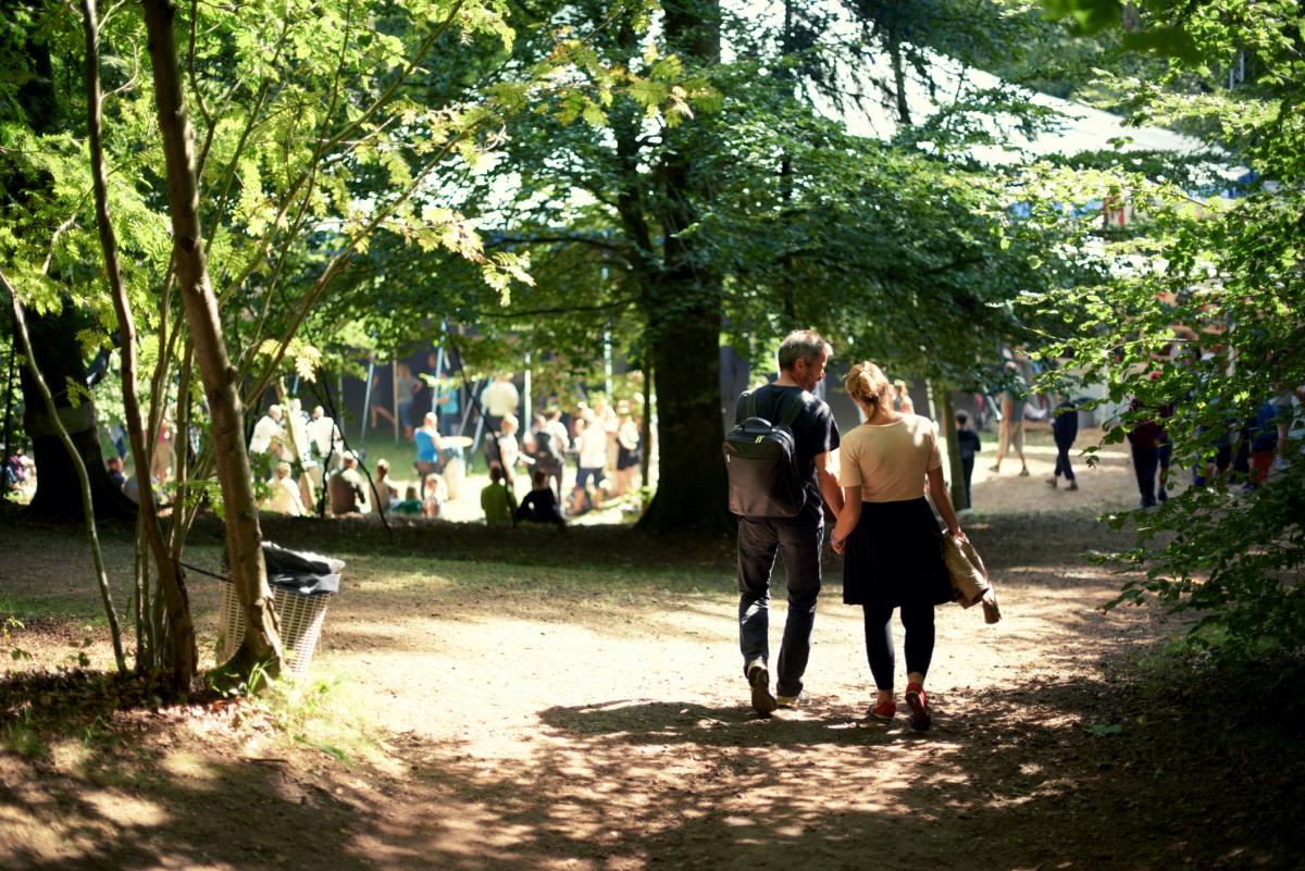 Couple walking in the forest next to a tent of festivities