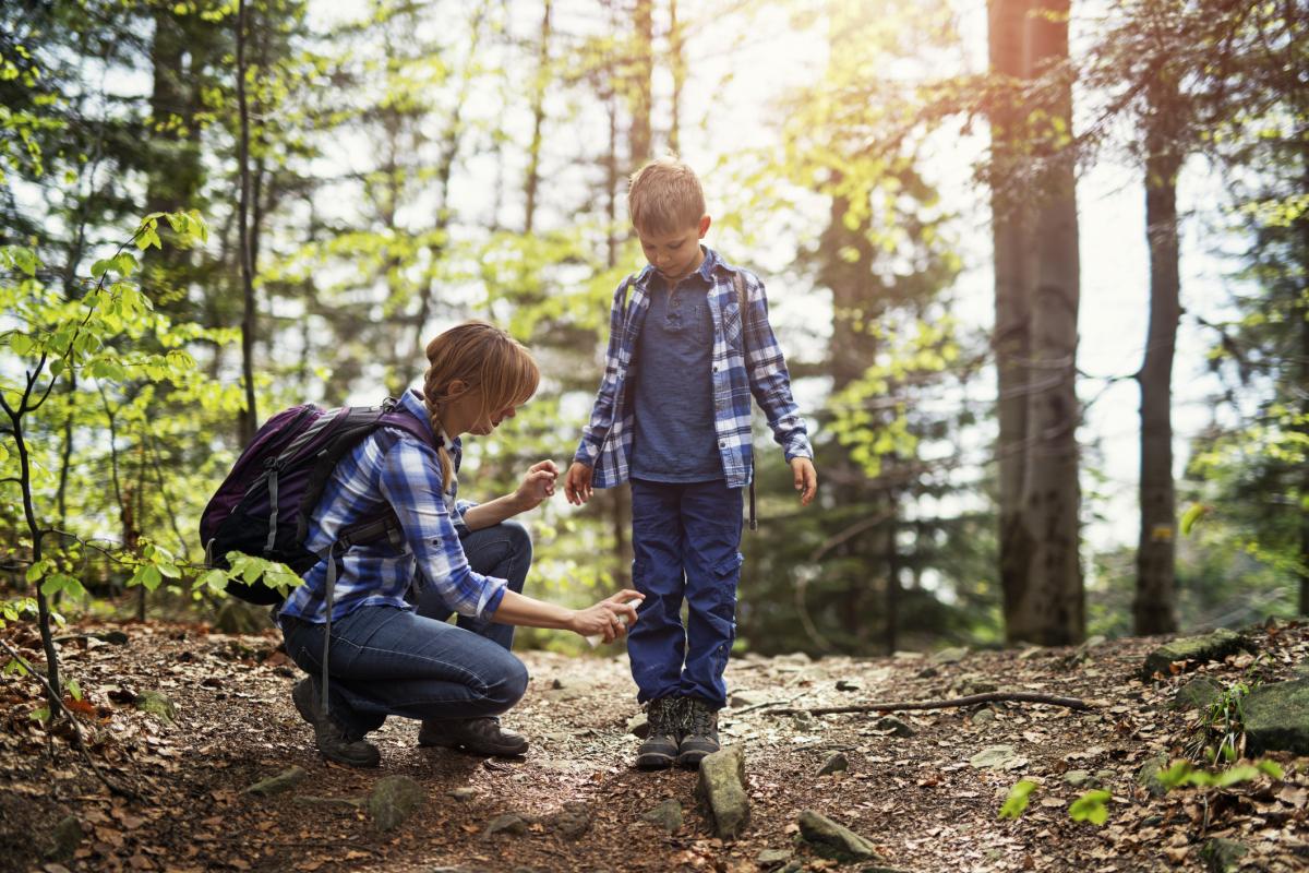 mom applying bug spray to her child, who is wearing long pants