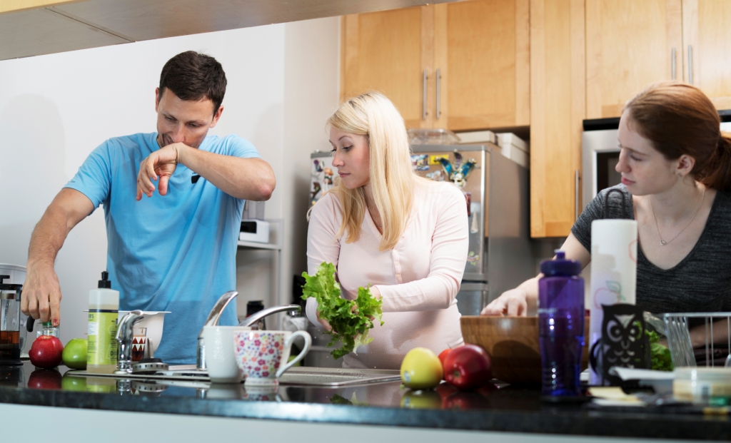 Pregnant woman and man cooking in the kitchen; the man is wiping his nose