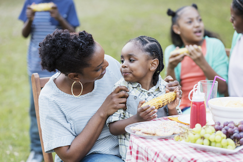 Woman with young girl on her lap eating at a barbeque