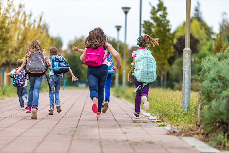 Group of children wearing backpacks running together away from the camera