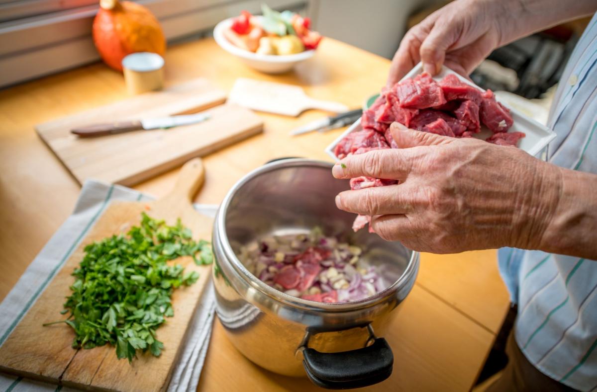 Hands of a senior person cutting meat to put into a stew
