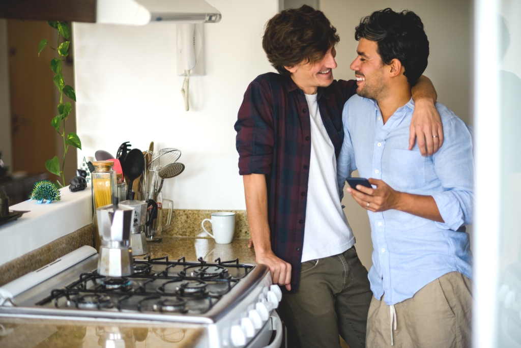 A couple nuzzling next to the stove in a kitchen