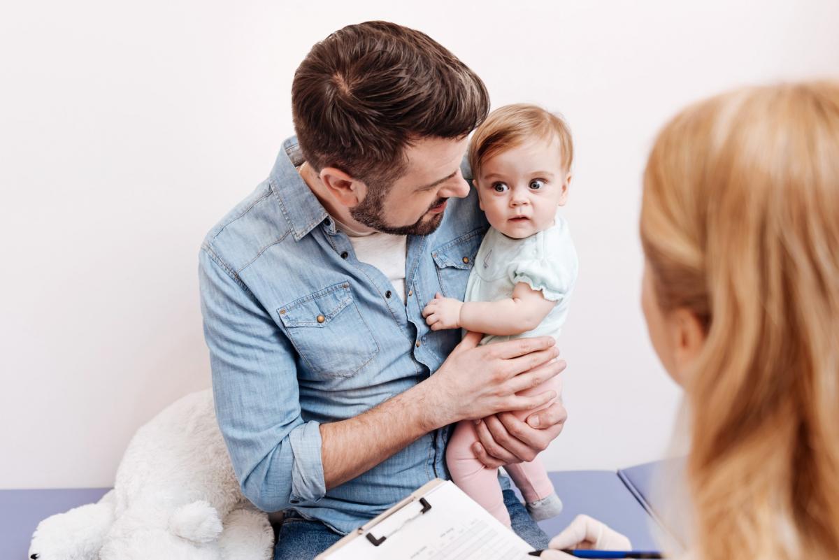 A dad cuddling his infant while a nurse fills out a form