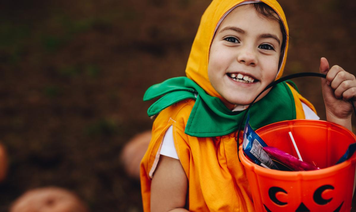 Young, happy child in a halloween pumpkin costume holding a bucket of candy.