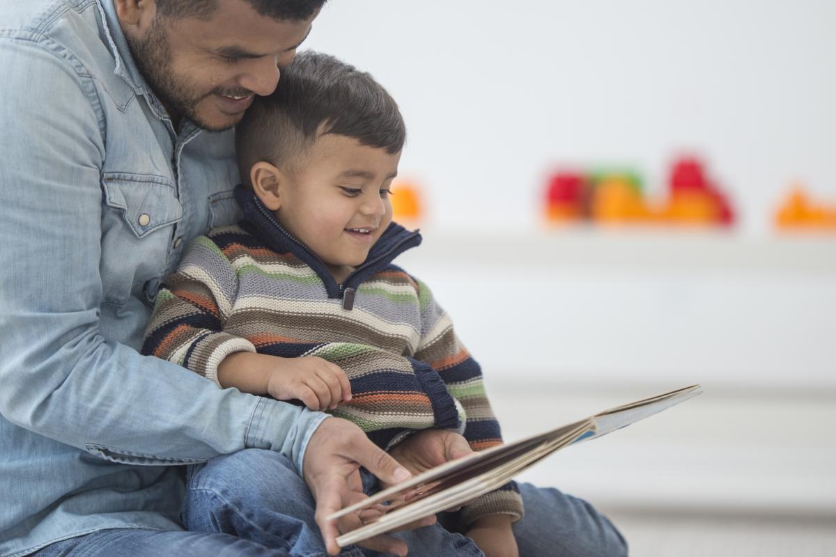 Little boy sitting in father's lap as they ready a book together