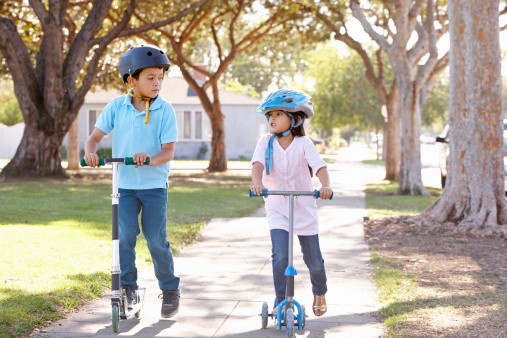 Two kids riding scooters outside