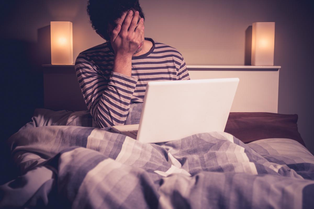 Man in bed with laptop holding head in hand