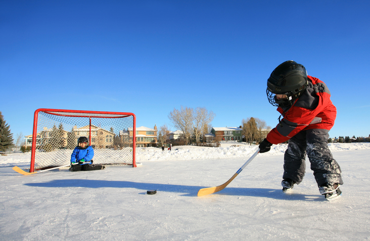 Two kids playing hockey outdoors on the ice