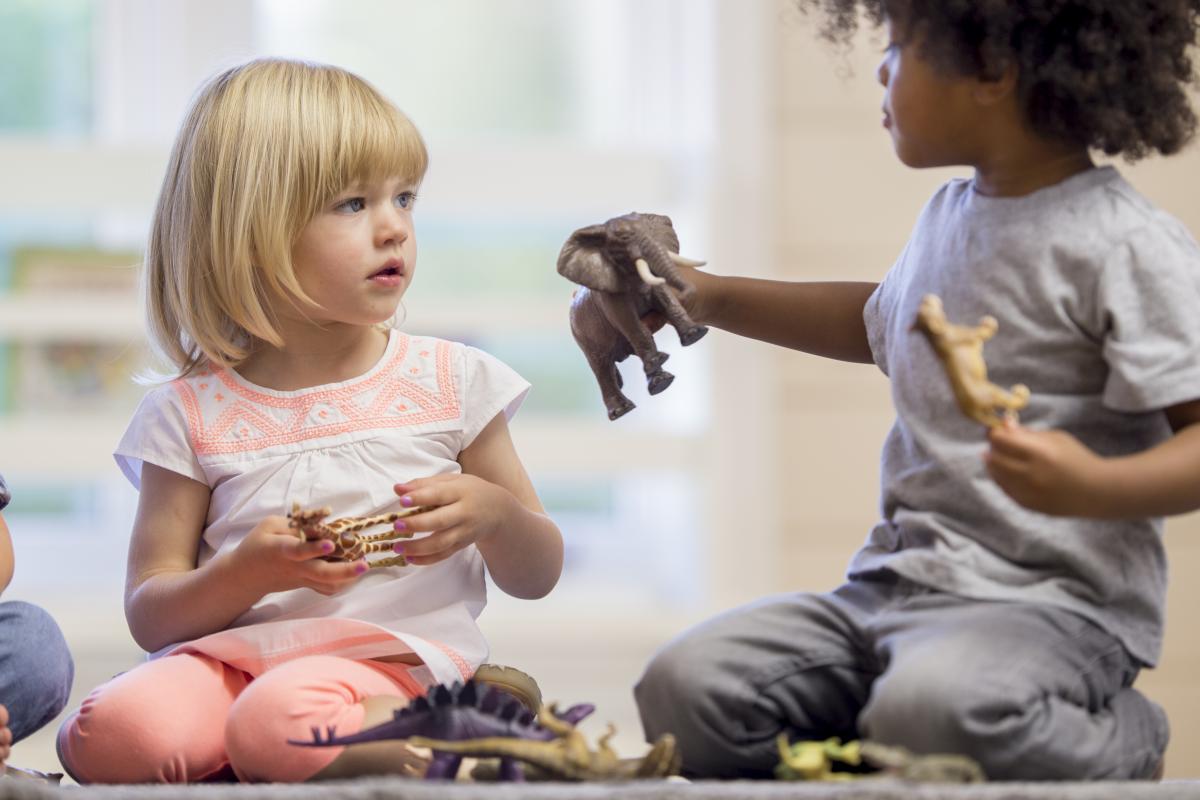 Two preschoolers sharing a dinosaur toy