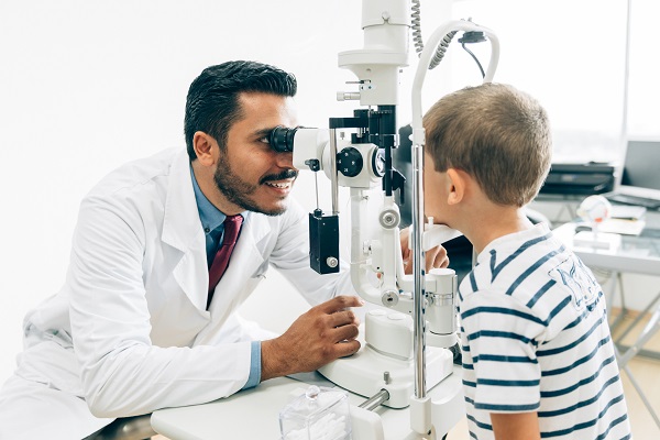 Optometrist looking through one end of a machine while a child looks through the other side