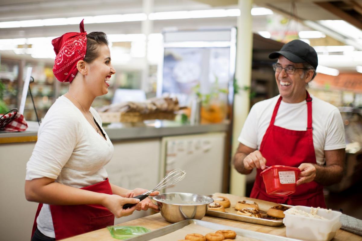 Two cooks whipping up donuts for a market and sharing jokes