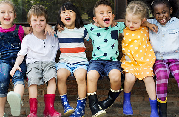 kids laughing sitting on a wall in rain boots
