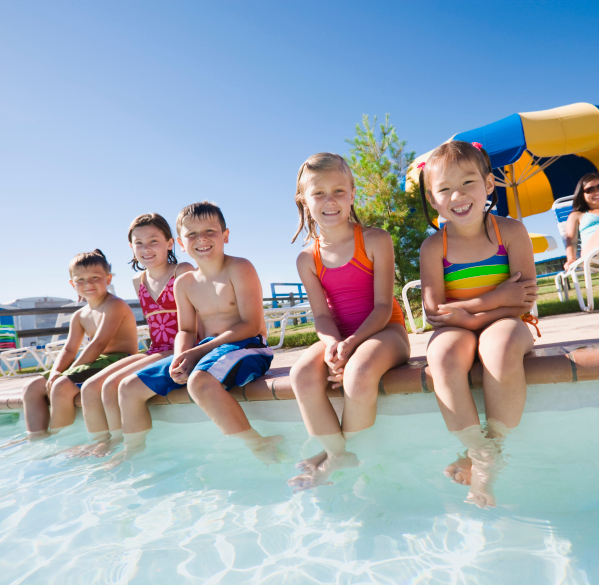 Group of kids sitting by side of pool smiling