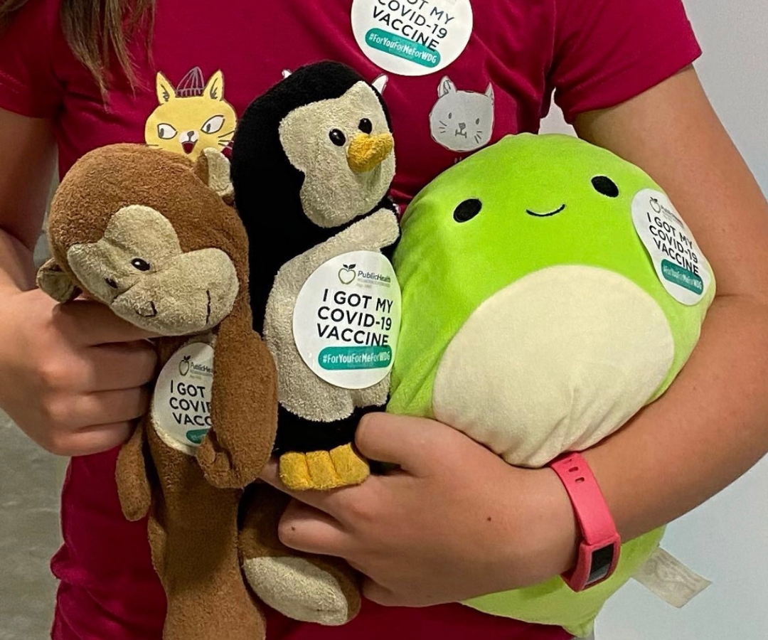 Person holding stuffed animals with stickers that say I got my COVID-19 vaccine.