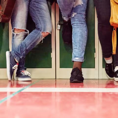 5 students standing in a row in front of lockers. Only legs and feet are shown