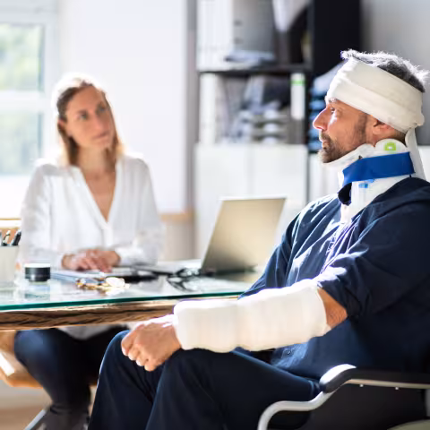 Injured man in casts and head bandages and neck brace talking to doctor
