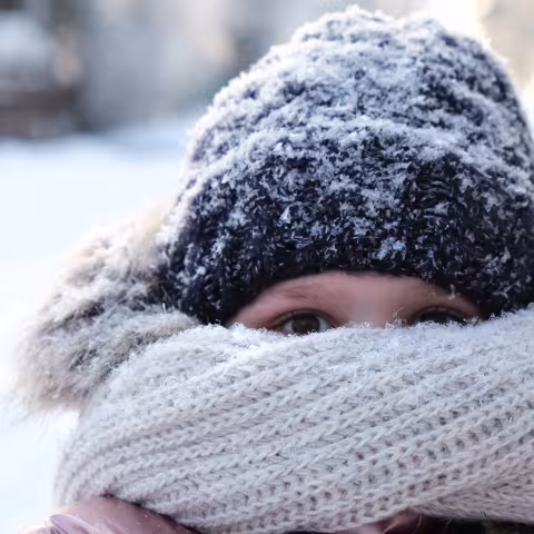 Young girl hiding her face with knitted bulky scarf during winter frost snowfall outdoors.
