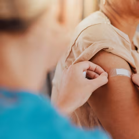 Someone getting a vaccine from a nurse, arm on bandaid