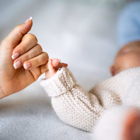 Close-up of mother's hand holding newborn baby's hand.