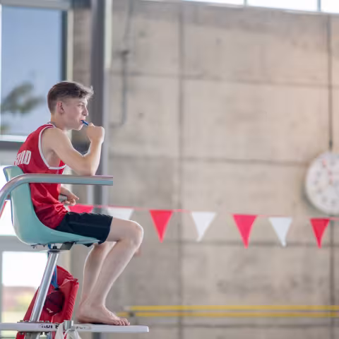 A lifeguard sits attentively at an indoor swimming pool, ensuring safety for swimmers. 