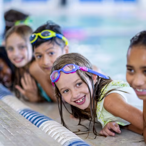 A multi-ethnic group of kids are indoors in a pool.