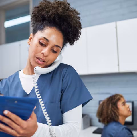 Female Healthcare Worker Taking Notes While Using a Phone in a Modern Medical Office