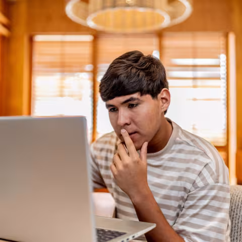 Teenage boy on laptop thinking
