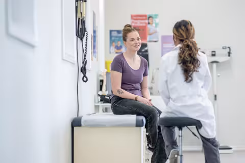 A young woman sits up on an exam table during a medical appointment