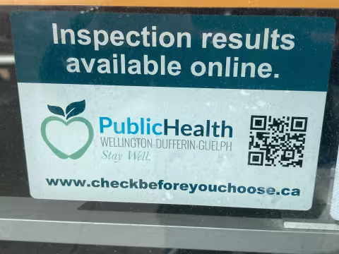 A sign promoting online public health inspections at the Check Before You Choose website with a QR code and the Wellington-Dufferin-Guelph Public Health logo.