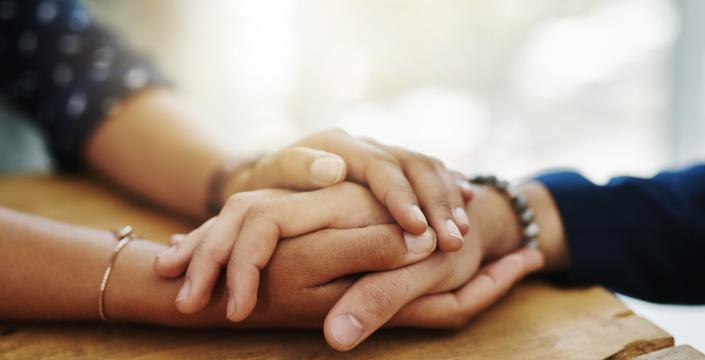 two people's hands shown on a table holding hands and providing comfort