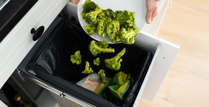 a plate of broccoli being scraped into the garbage