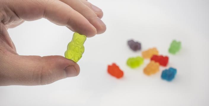 hand holding gummy bear candy with more candies sitting on the table behind