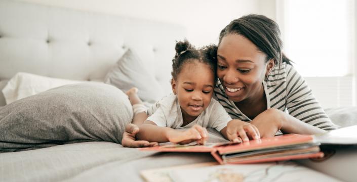 mother and toddler lay on the bed together reading a book