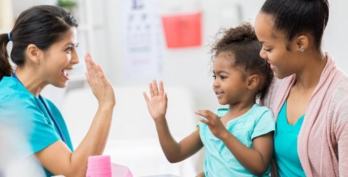 Vaccine success! A child giving a doctor a high five while sitting on her mom's lap