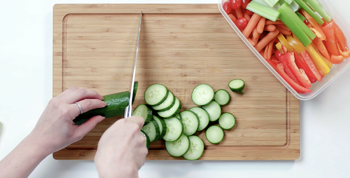 An birds-eye view of someone's hands slicing cucumbers on a cutting board