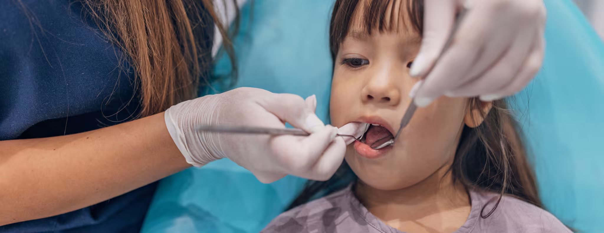 Female dentist examining her little girl patient teeth in dentist's office.