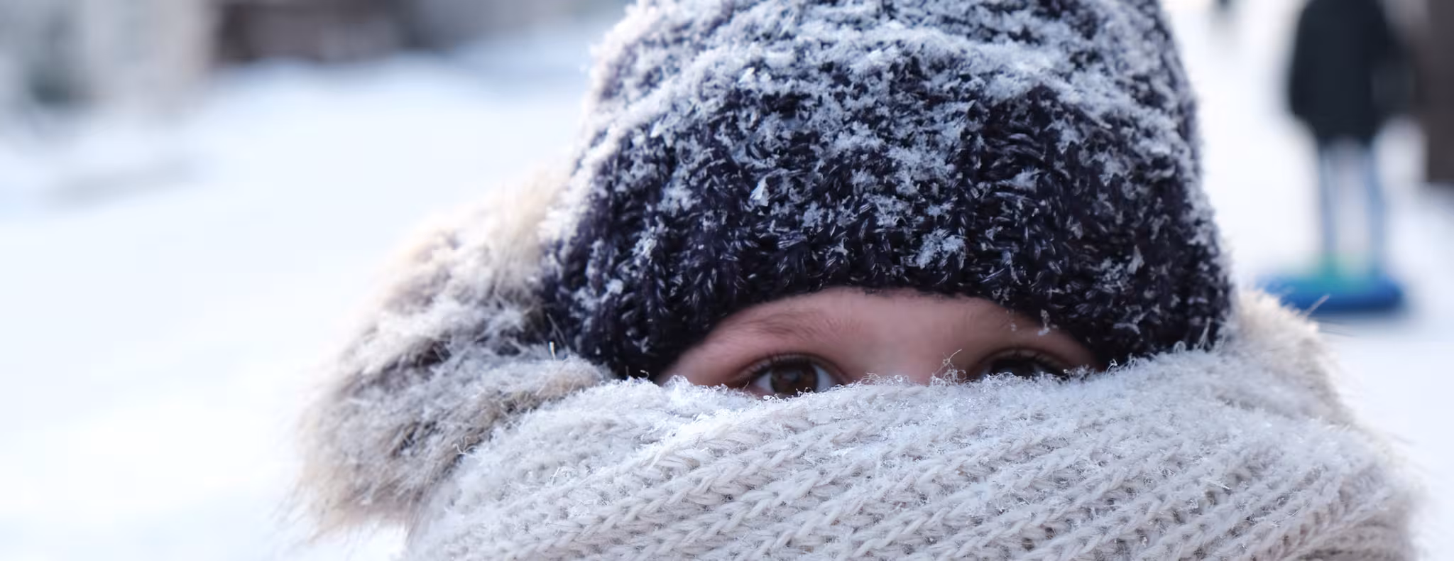 Young girl hiding her face with knitted bulky scarf during winter frost snowfall outdoors.