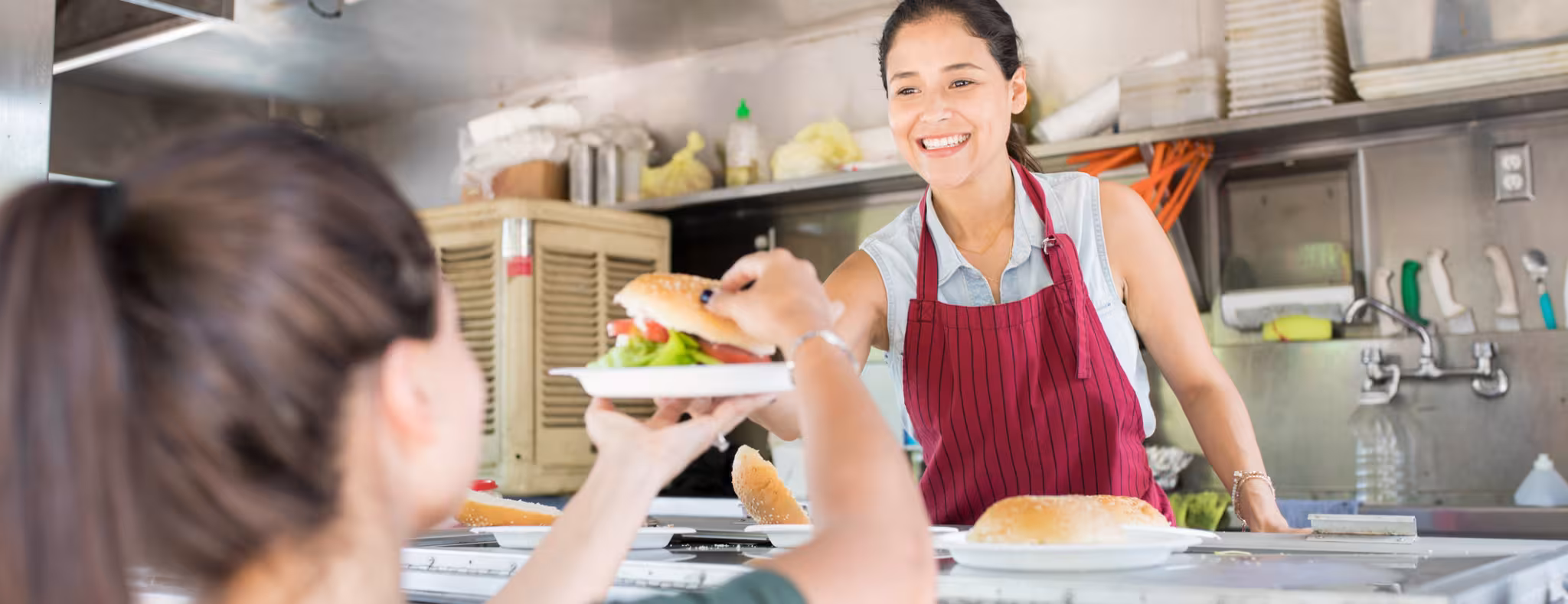 Portrait of a gorgeous young woman working in a food truck and selling hamburgers with a smile