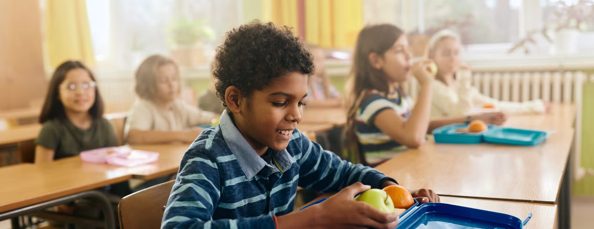 Happy black boy having fruit for snack during a break in the classroom