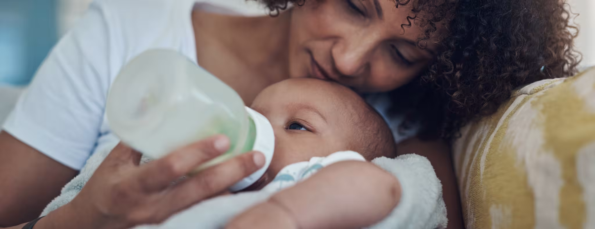 dorable baby girl being bottle fed by her mother on the sofa