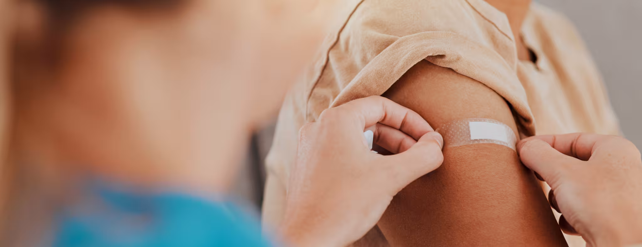 Someone getting a vaccine from a nurse, arm on bandaid