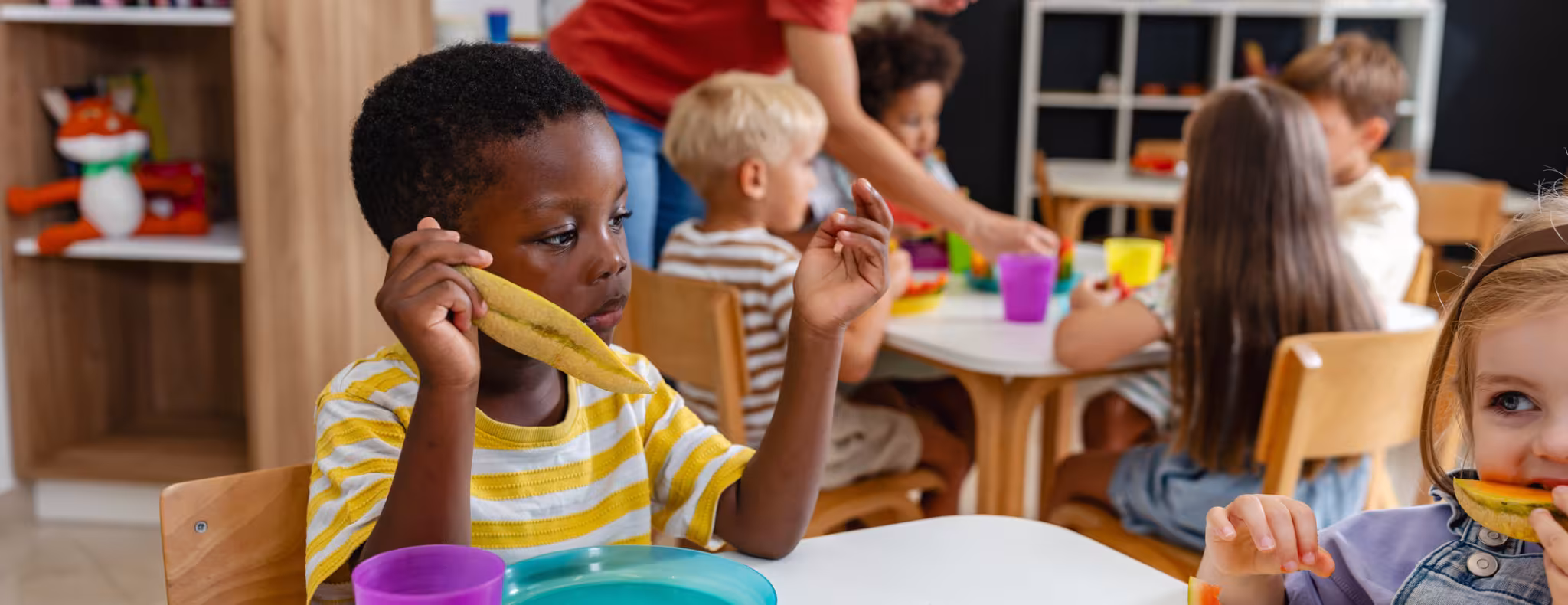 Preschool children sitting at a table eating fresh watermelon slices during snack time