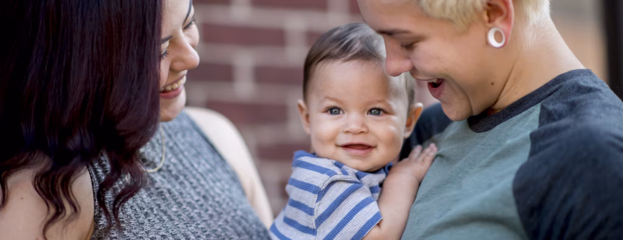 Young same sex couple adoringly smile at their baby boy