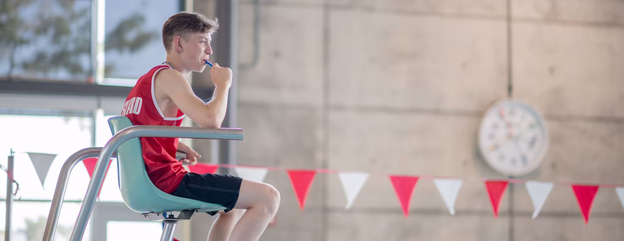 A lifeguard sits attentively at an indoor swimming pool, ensuring safety for swimmers. 