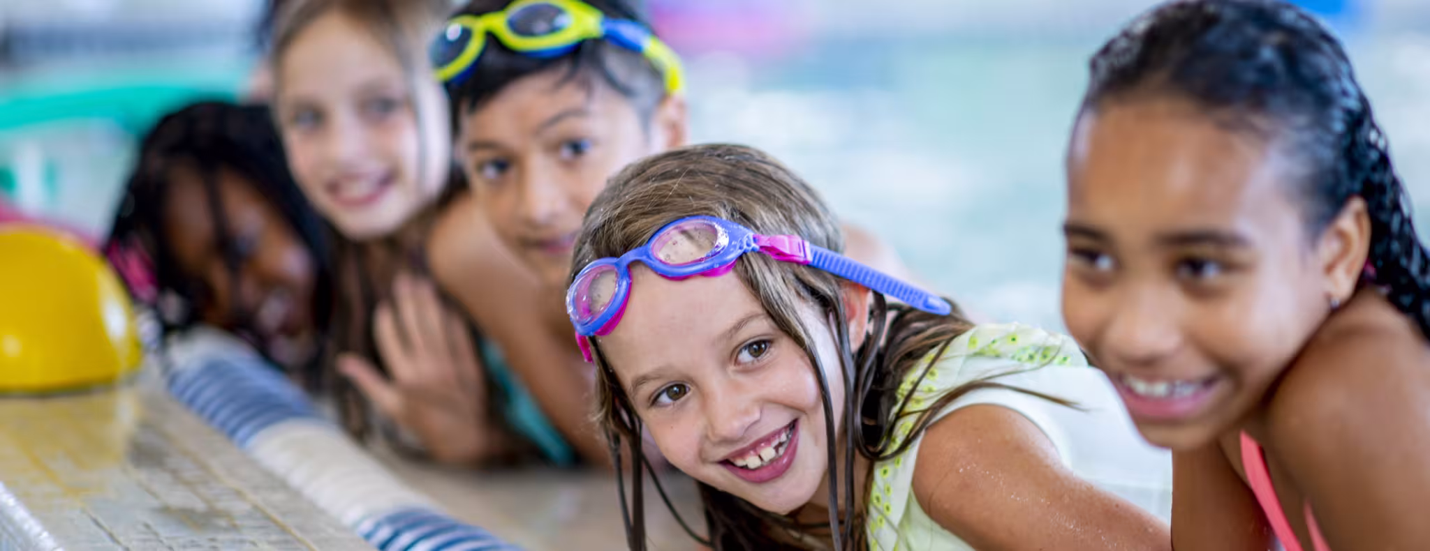A multi-ethnic group of kids are indoors in a pool.
